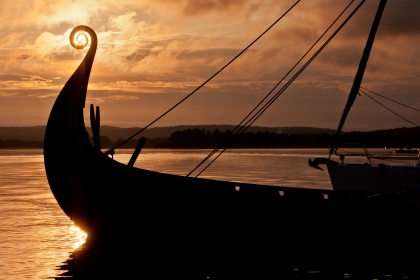 Viking boat sails on water in yellow sunset